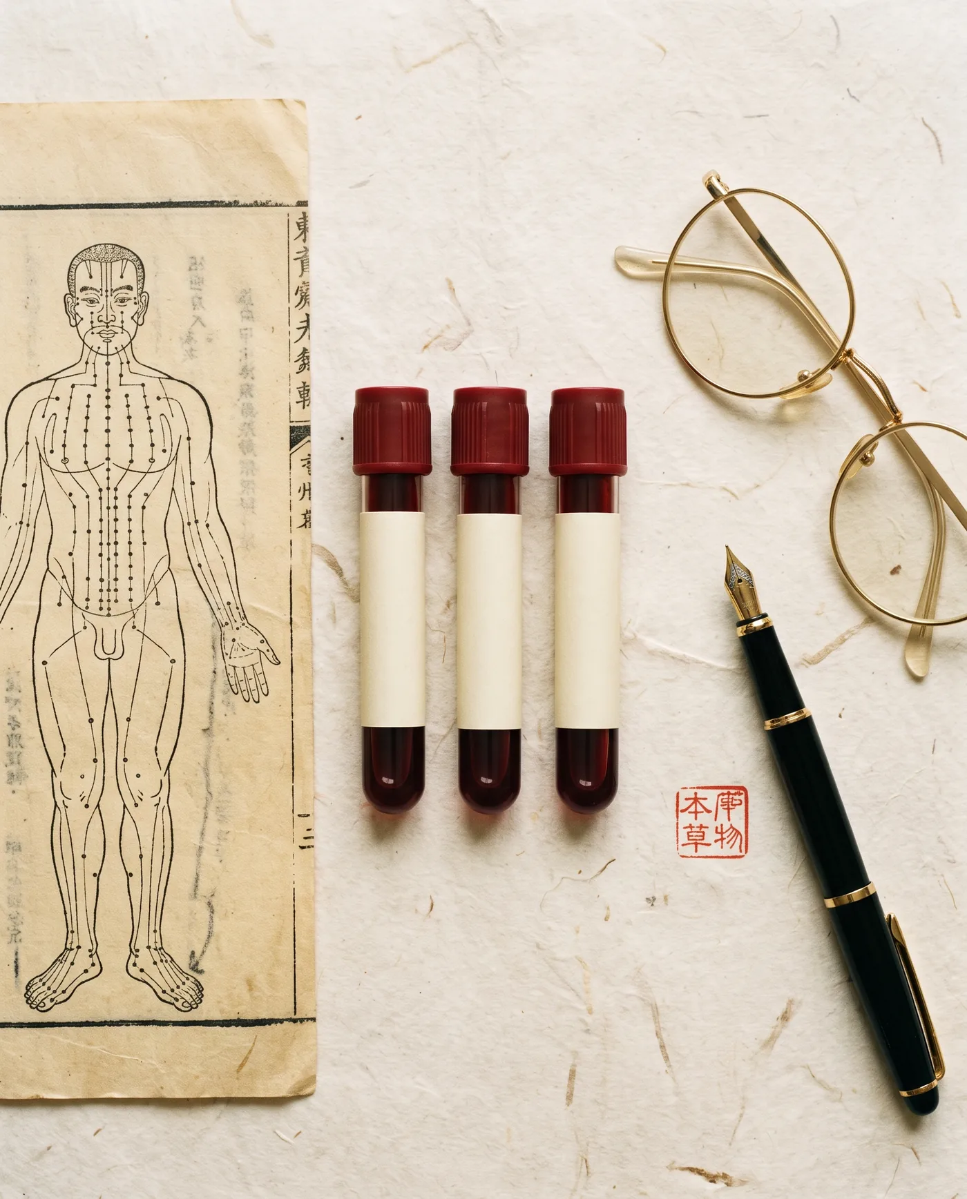 Three blood vials beside an antique meridian chart, a pen, and reading glasses.